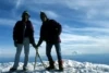 An old photo of two people standing on a snowy mountain top with ice axes.