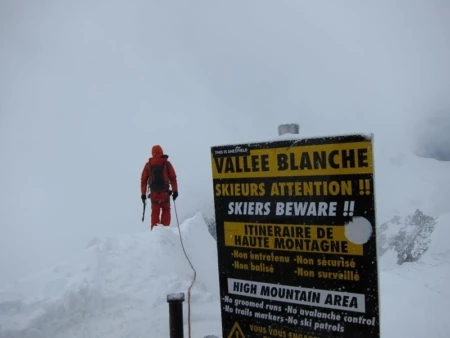 A roped-up climber walks past a sign in French that roughly says Beware!