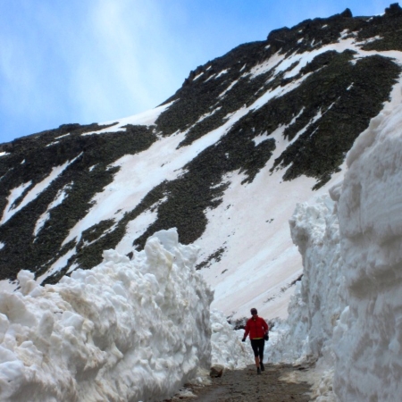 A person runs on a plowed road in between two massive snow walls.