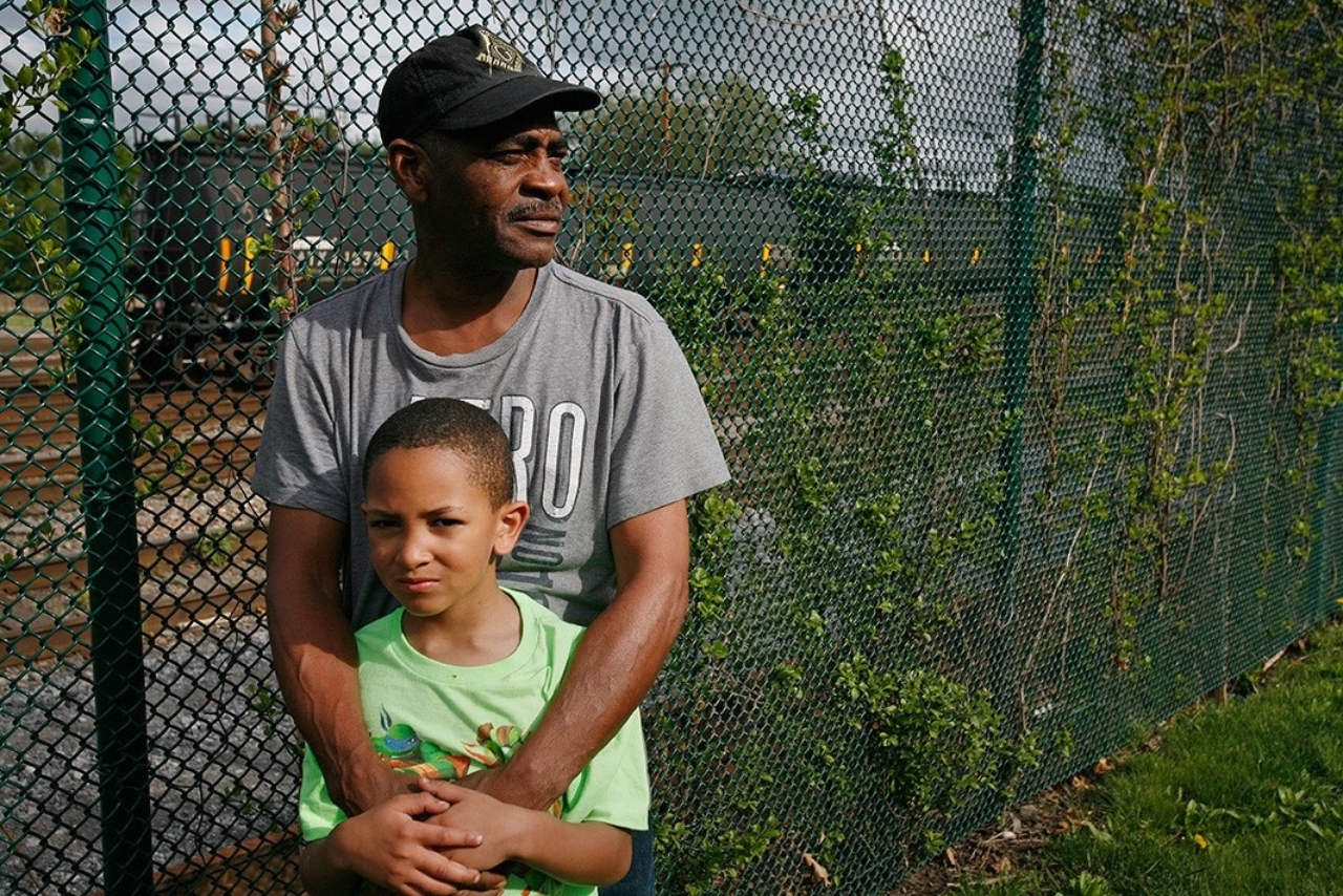 Be Be White and his son Brayton stand along the fence that separates the railroad tracks from Ezra Prentice Homes. Albany, New York. Photo: Earthjustice