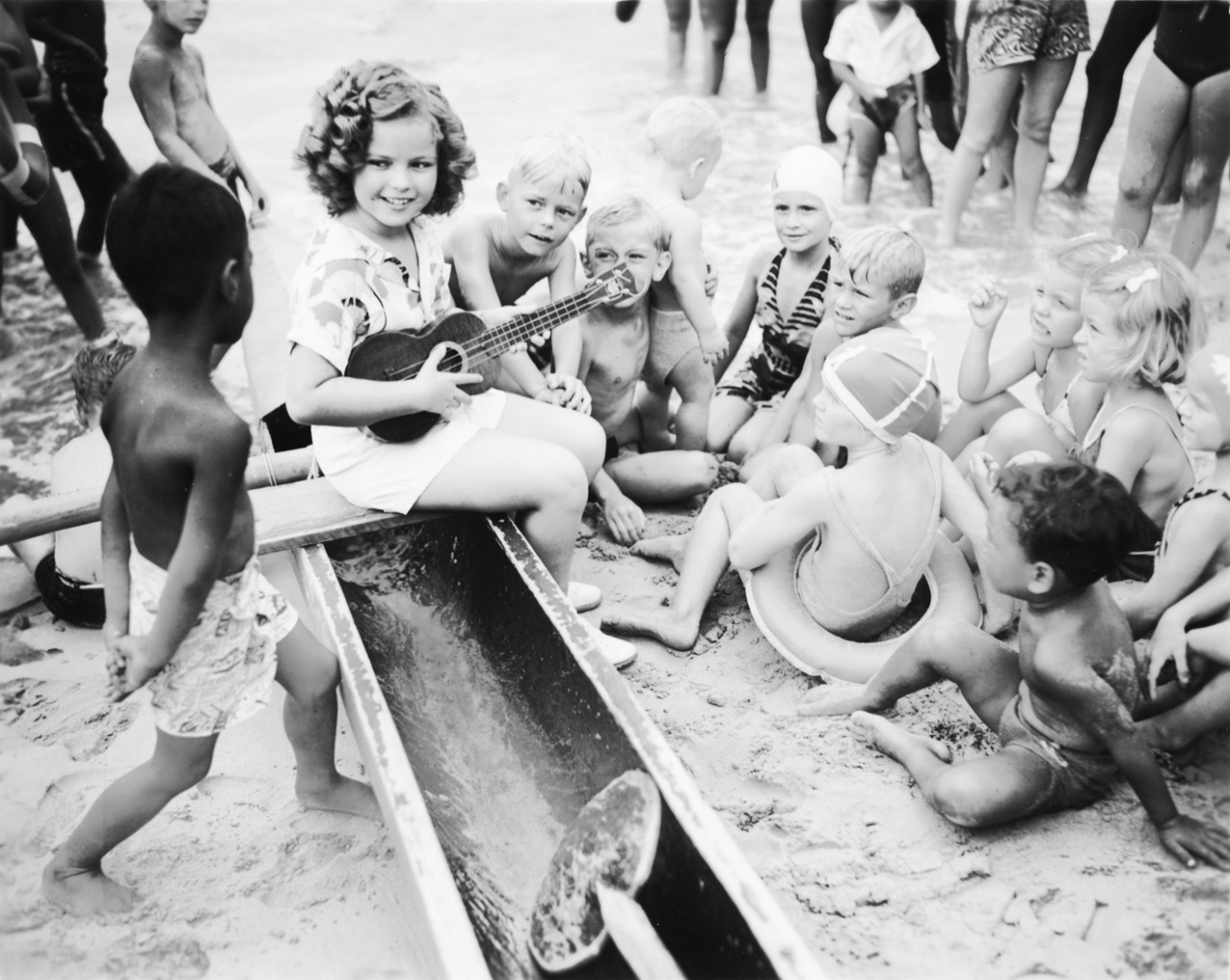 Shirley Temple, wearing an early Kabe crepe aloha shirt, playing her ‘ukulele with the local children on Waikiki Beach. Photo courtesy of the Bishop Archives