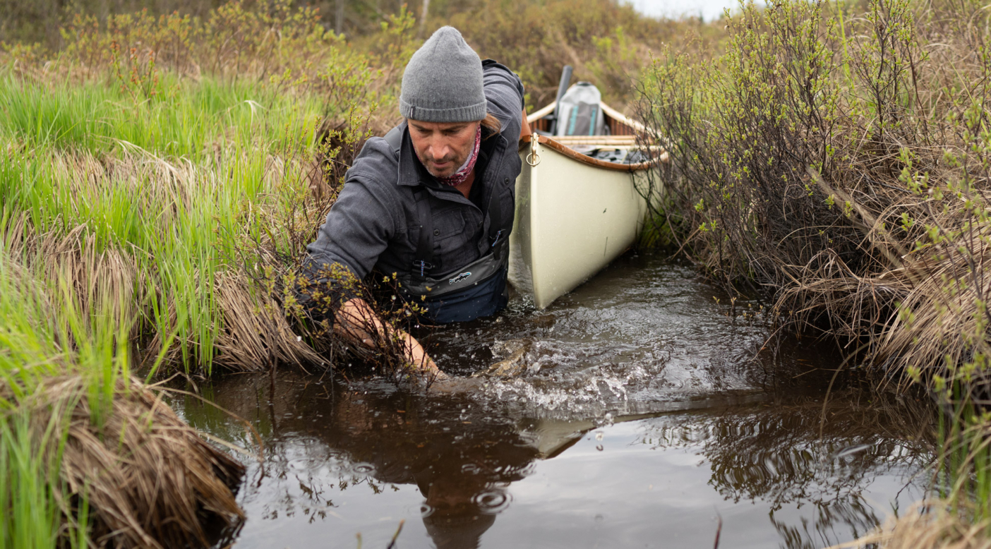 Boots in the water and paddle on the bow seat, Nathaniel Riverhorse Nakadate navigates a tight, soggy portage. TONY CZECH