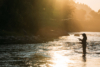 A person standing in a river casting their fly rod with the sun low on the horizon.