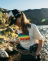 A person with long brown hair wearing a white t-shirt with a rainbow graphic.